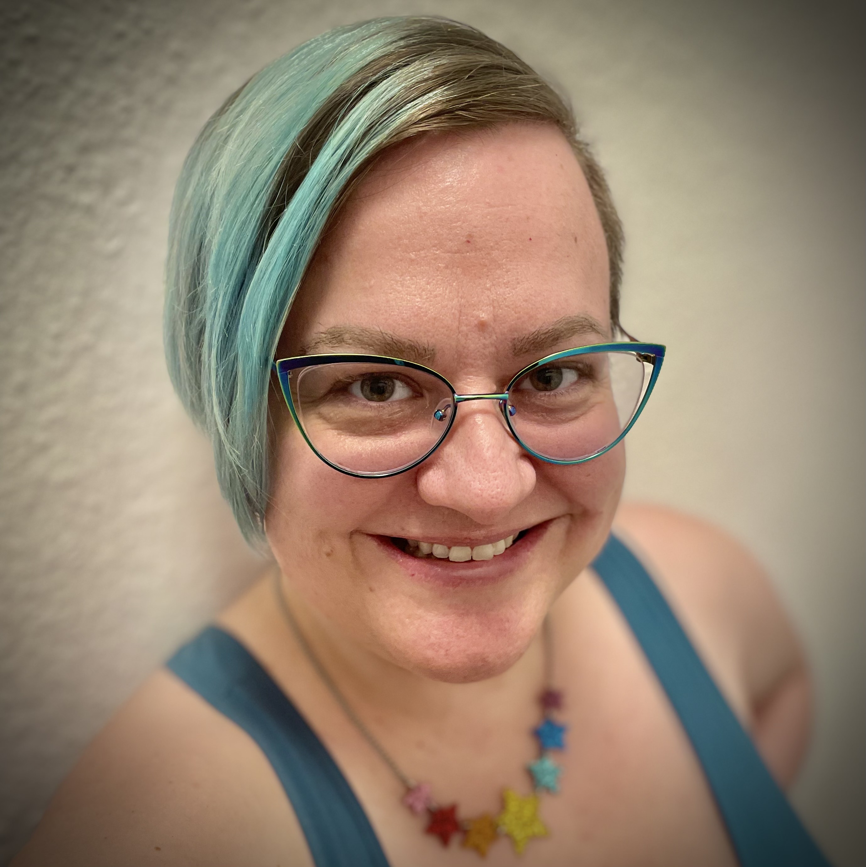 Biddy is a queer, white woman with glasses, blue hair, and a rainbow necklace.